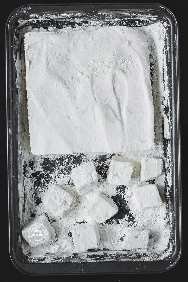 A block of marshmallows on a baking tray and some marshmallow cubes.