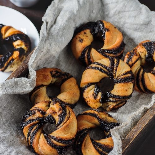 six small poppy seed buns shaped like donuts on a linnen cloth.