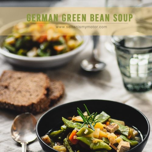 Two plates of green bean soup on a tablecloth with glasses and a slice of bread.