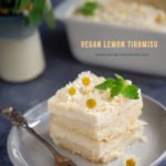 A slice of vegan lemon tiramisù on a plate with some flowers in the background.