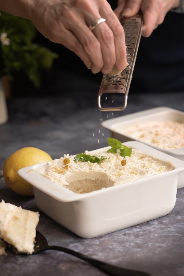 A dish filled with vegan tiramisu and a hand that sprinkles some white chocolate on top.