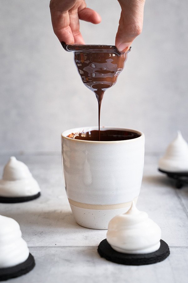 Eine Tasse mit flüssiger Schokolade, in die ein Schokokuss eingetaucht wird.