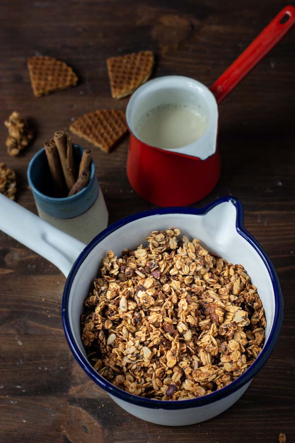 Eine Tpf Granola auf einem Tisch, dazu Sojamilch und Zimtstangen.