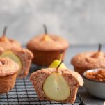 Wholesome vegan pear muffins on a tray. One muffin is sliced in half to reveal the pear.