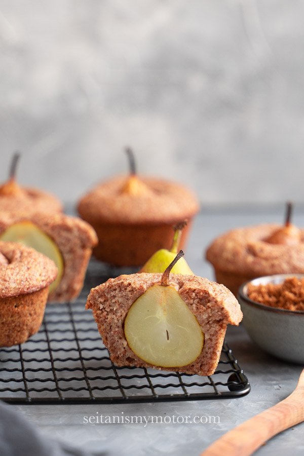Wholesome vegan pear muffins on a tray. One muffin is sliced in half to reveal the pear.