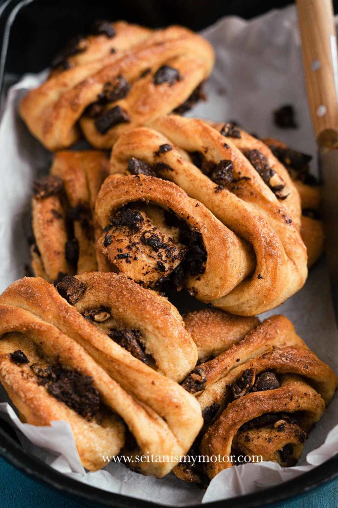 A couple of franzbrötchen on white parchment paper in a baking tray.