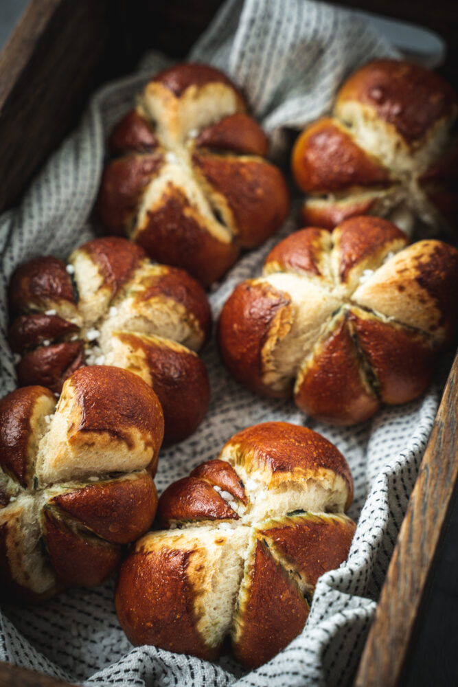 Six pieces of pumpkin shaped pretzel rolls on a napkin in a wooden box.