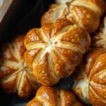 A couple of pumpkin shaped pretzel rolls in a wooden box.