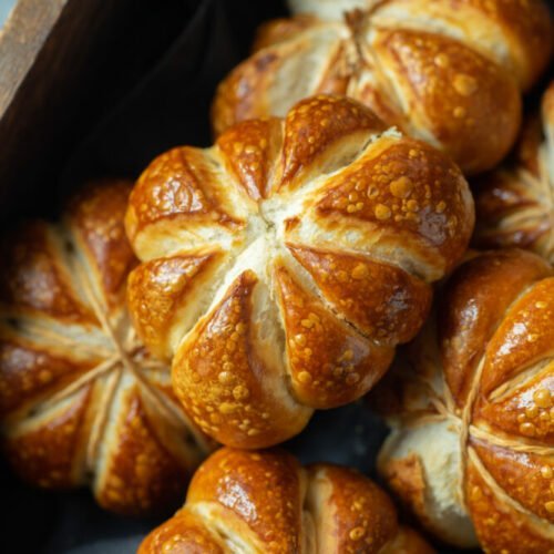 A couple of pumpkin shaped pretzel rolls in a wooden box.