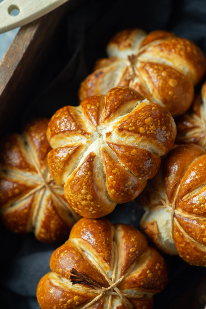 A couple of pumpkin shaped pretzel rolls in a wooden box.