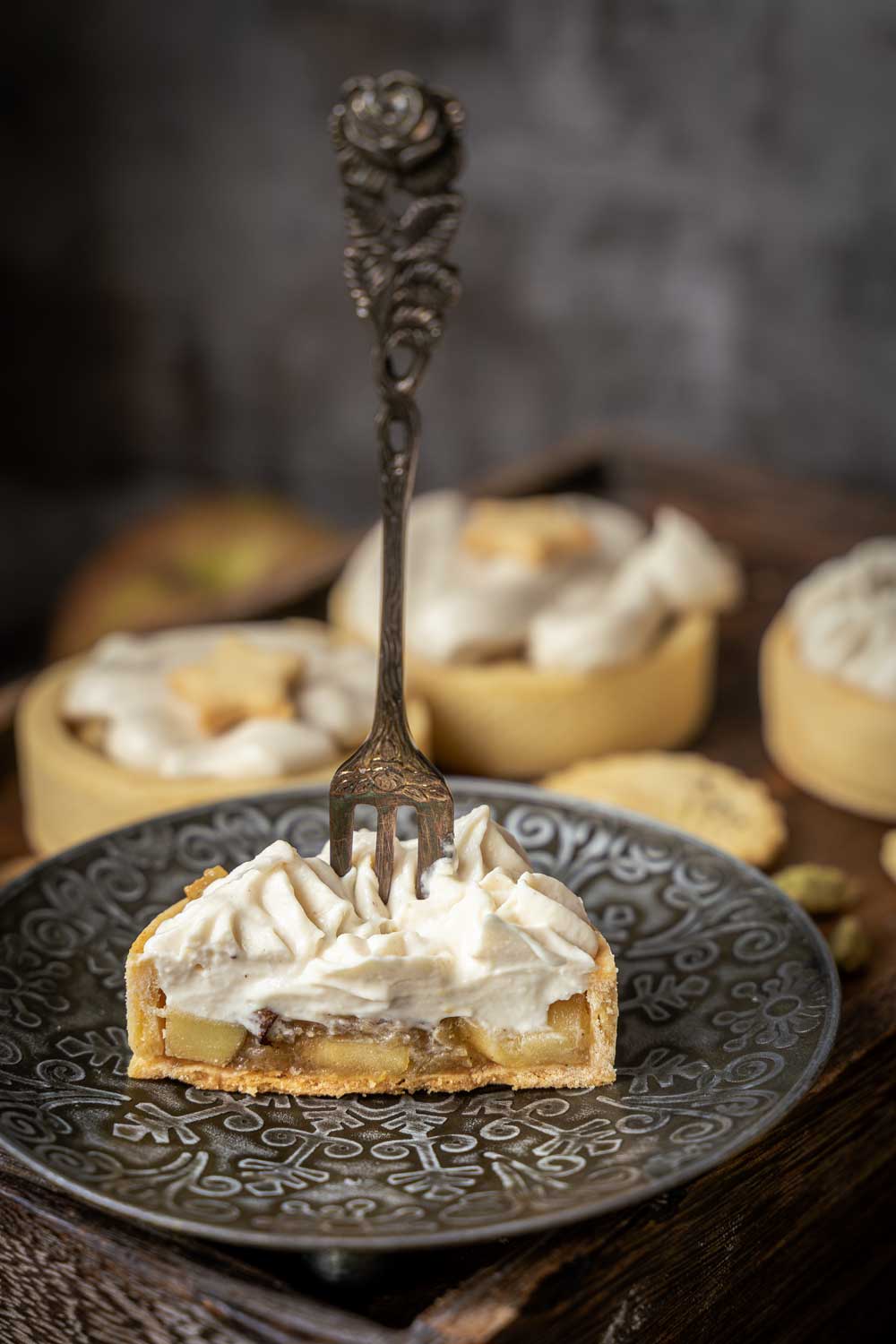 Apple tartlets with shortbread crust, cut in half on a small silver coloured plate. The apple tartlet is topped with vegan whipped cream.